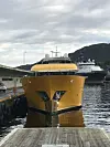 Gul yacht ved kai i havn med fjell og annet skip i bakgrunnen.