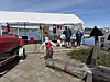 Barn i redningsvest løper foran telt med stand ved småbåthavn.