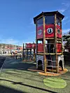 Leketårn i tre og rødt plast på lekeplass ved marina i solskinn