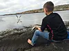 Person sitter på svaberg ved sjøen med fiskestang og måker over vannet.