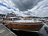 Stor motorbåt fortøyd ved brygge i småbåthavn med skyet himmel.