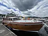 Stor motorbåt fortøyd ved brygge i småbåthavn med skyet himmel.