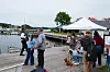 Folk danser og spiller trekkspill ved en brygge med hvitt telt og småbåter i bakgrunnen.
