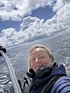 Person tar et selfie på en båt med hav og skyfylt himmel i bakgrunnen.