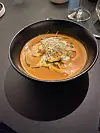 Svart bolle med oransje kremet suppe toppet med spirer på et mørkt bord.