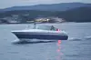 Hvit og blå motorsbåt på rolig vann med fjell og lysspor i bakgrunnen.