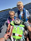 To barn sitter i en båt med en kosebamse foran seg på sjøen.