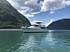 Hvit motorbåt på stille fjord med fjell og skyer i bakgrunnen.