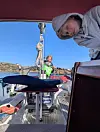 Barn i hettegenser om bord på seilbåt med voksen i bakgrunnen og havutsikt.