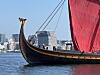 Vikingskipet Harald Hårfagre med stort rødt seil på vannet foran silhuetten av Oslos waterfront.