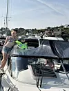 Ung jente står på en motorbåt i en havn med andre båter og hus i bakgrunnen.