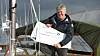 Seiler holder et dokument på en seilbåt i en marina.