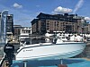Hvit motorbåt med Suzuki-motor ved en byhavn, med lystbåter og bygninger i bakgrunnen.