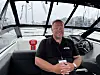 Mann sitter i førersetet på en motorbåt i en marina.