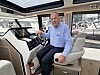 Mann ved roret i en moderne motorbåt med navigasjonsskjerm og utsikt over marinaen.