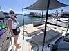 Kvinne med solbriller på en båt i en solfylt marina.